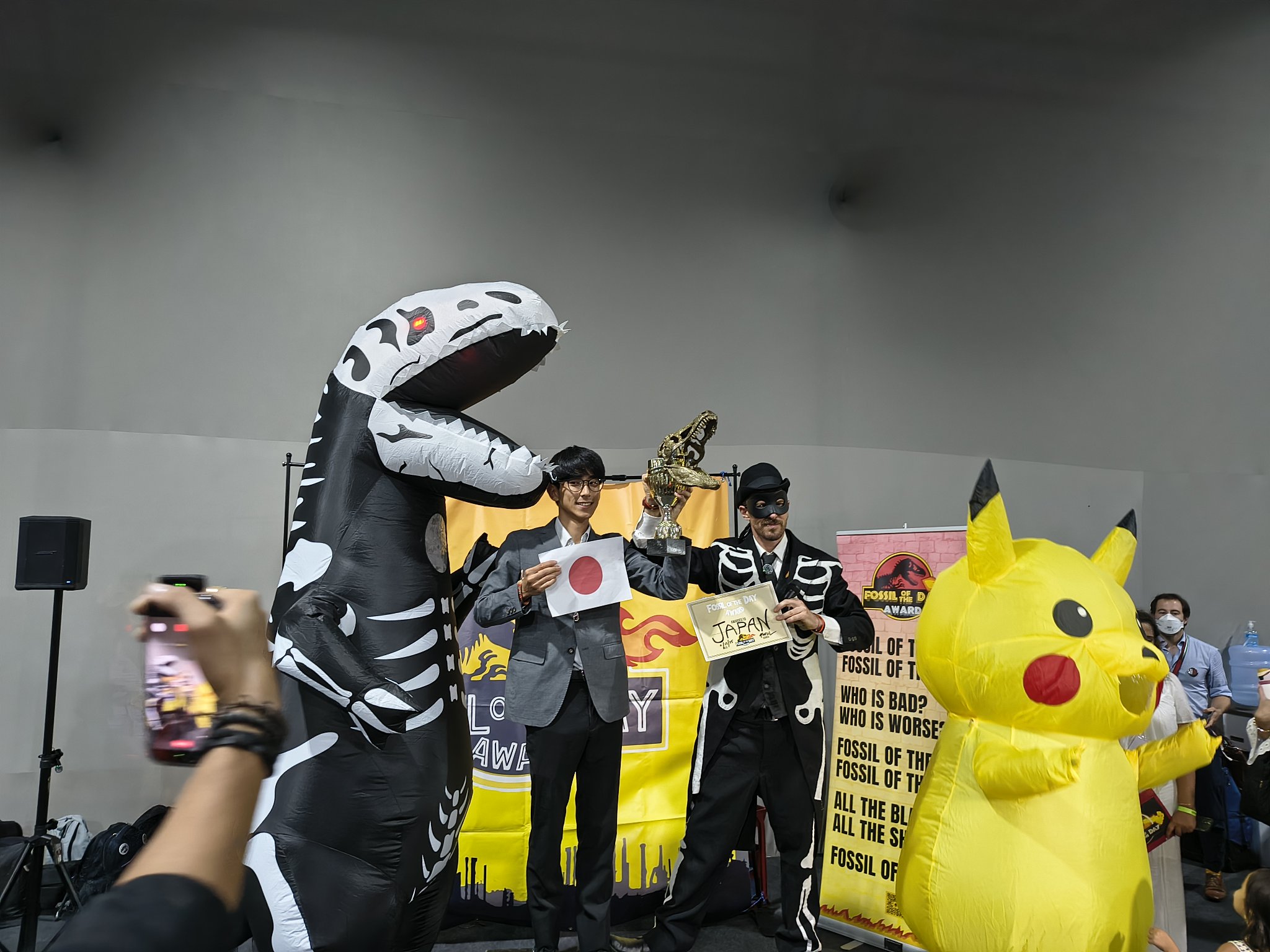 COP30の授賞式で、日の丸とJAPANの賞状を手に立つ人と、恐竜の骨の着ぐるみ