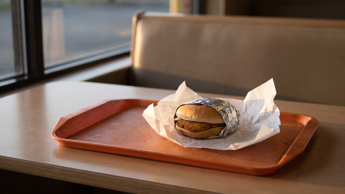 ファストフード店のトレーに、包み紙に入ったチキンバーガーが1つだけ置かれている場面