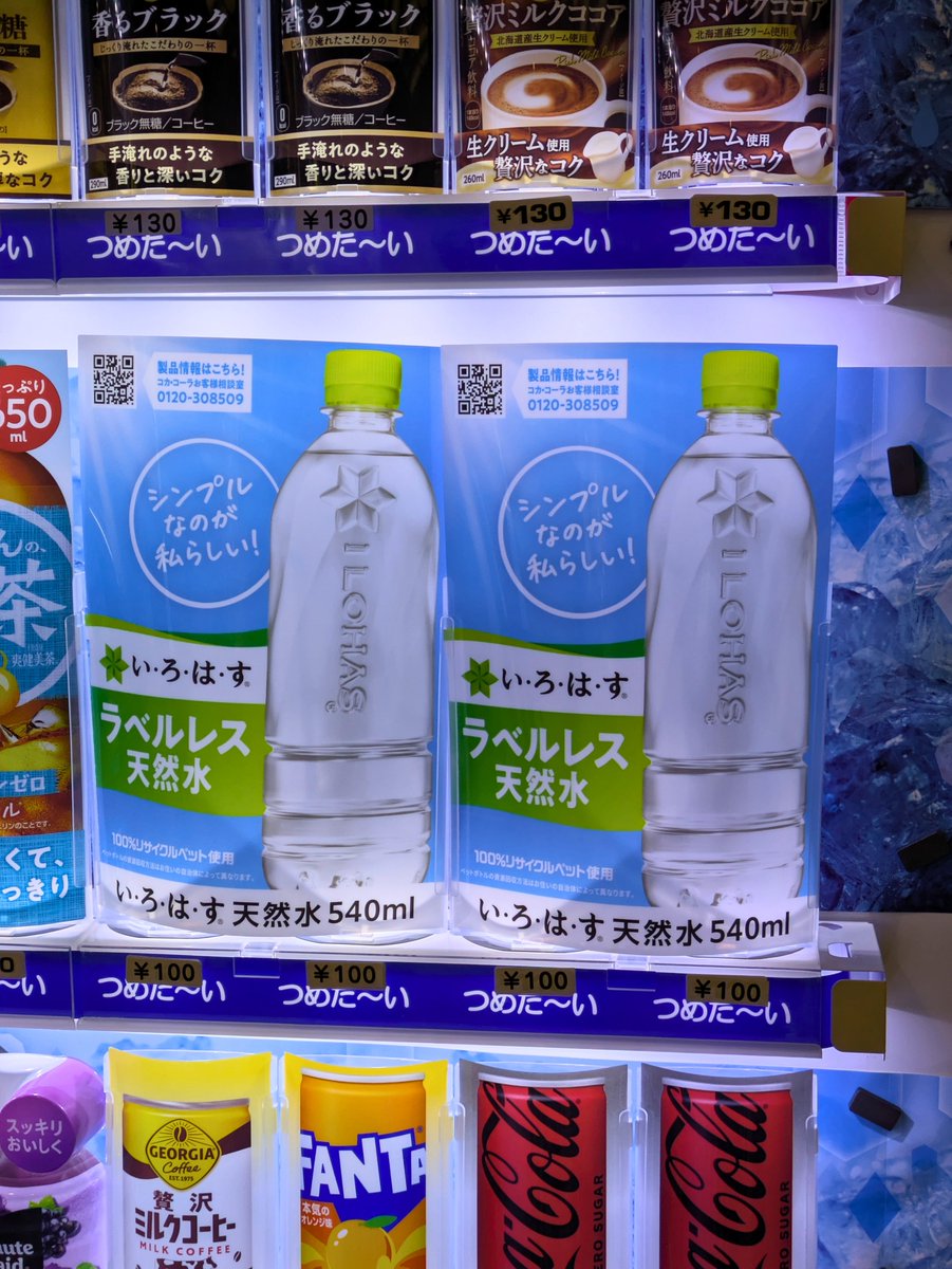 自販機に並んだ「い・ろ・は・す ラベルレス天然水540ml」の見本。製品情報のQRコードとお客様相談室の電話番号が付いている