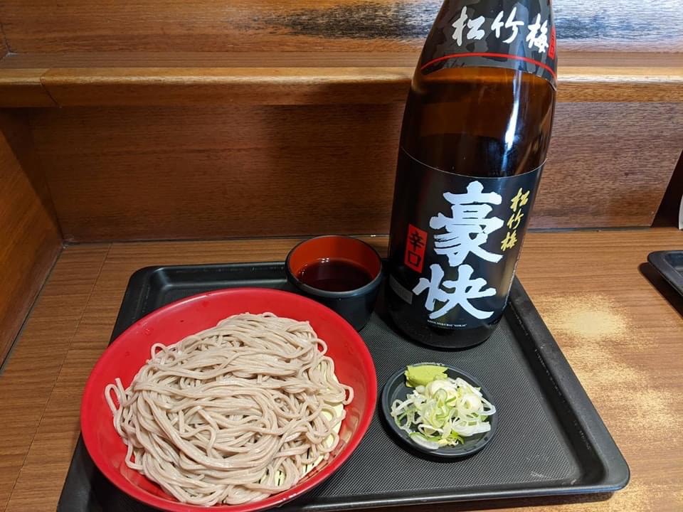 赤い器に盛ったもりそばと、つゆ、ねぎとわさび、辛口の日本酒（松竹梅 豪快）の瓶