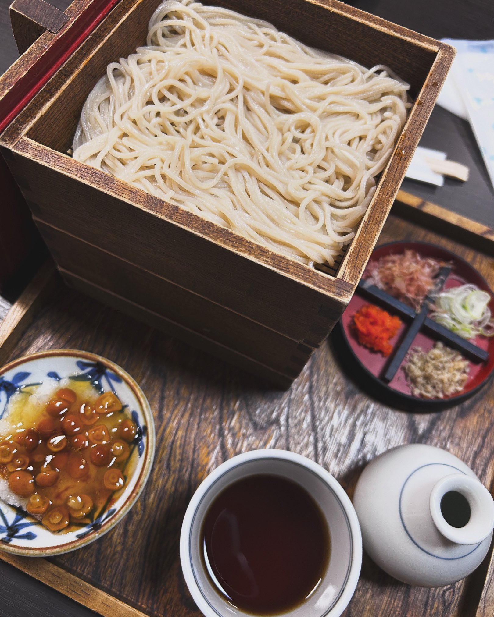 せいろのそばと、そばつゆ、なめこおろし、4種の薬味、白いとっくりがお盆に並んでいる