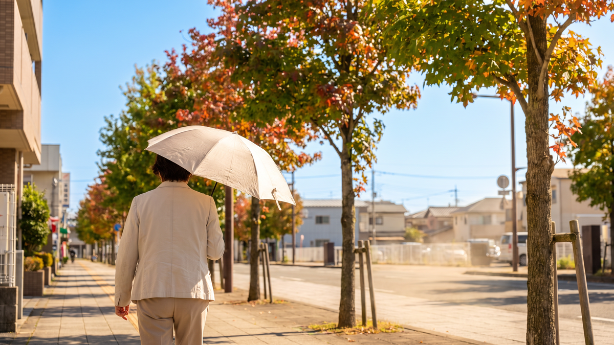 秋の街角で強い日差しの中、日傘をさして歩く人